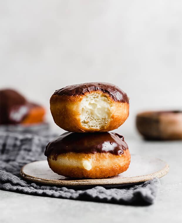 Two Boston Cream Donuts stacked on top of one another with the top donut having a bite taken out of it.