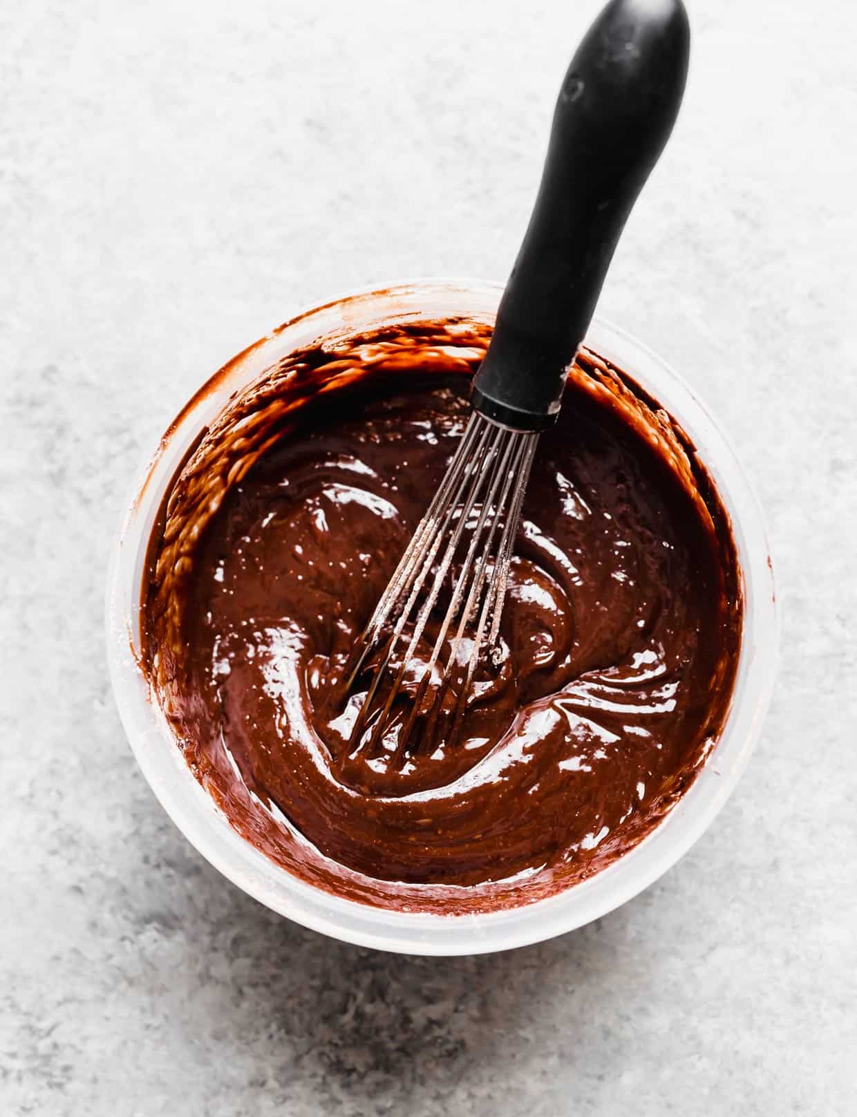 A melty chocolate glaze in a bowl with a whisk in it.
