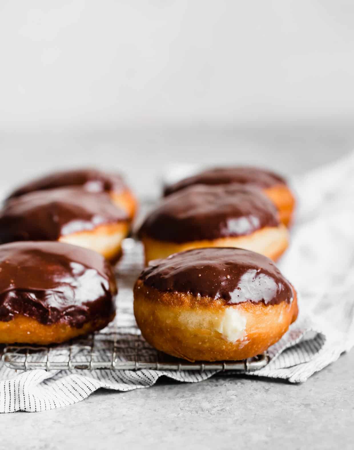 Pastry cream filled Boston Cream Donuts on a wire rack on a grey background.