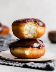 Two Boston Cream Donuts on a white plate against a light grey background.