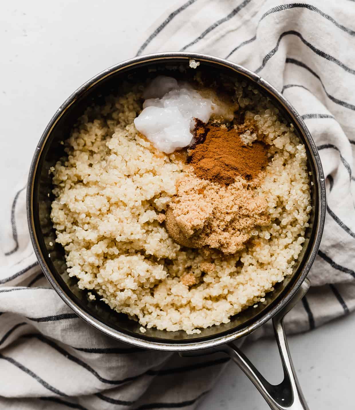 A small pot with cooked quinoa, ground cinnamon, and brown sugar.