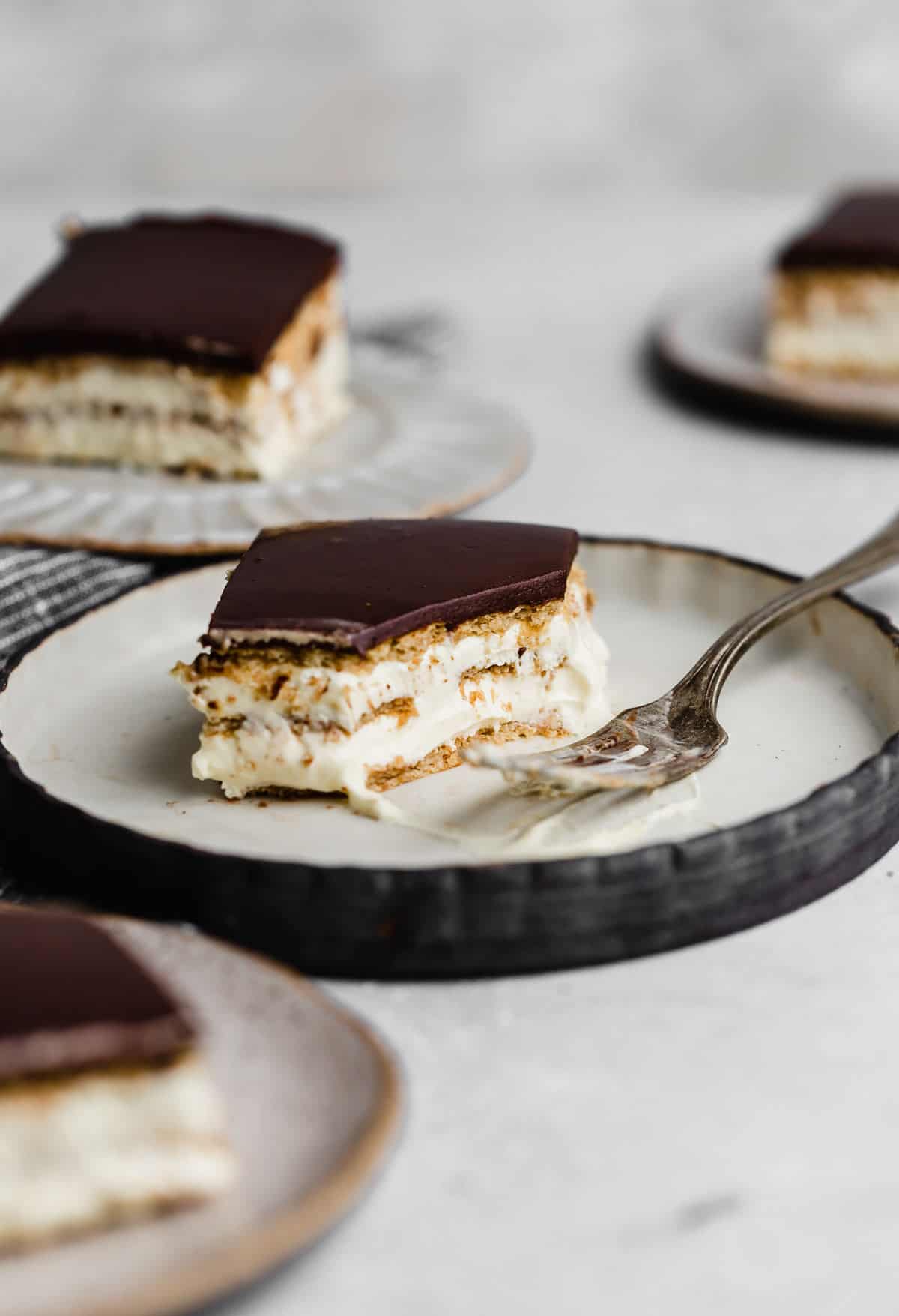 A no bake Chocolate Eclair Cake made with alternating layers of graham cracker and instant pudding (topped with chocolate) on a plate.