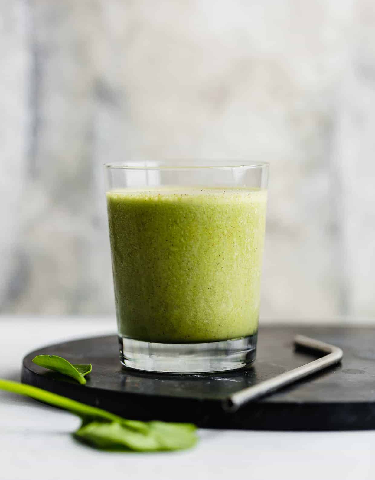 A green smoothie in a cup with spinach leaves in the foreground.