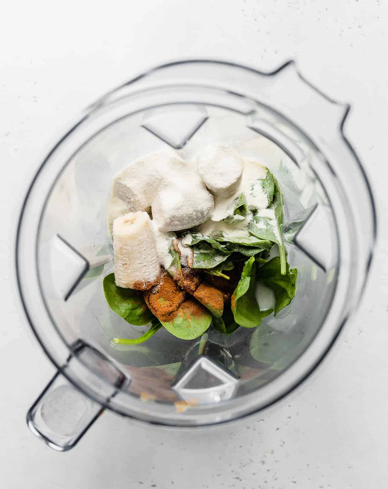 Overhead photo of a blender loaded with spinach, bananas, and ground cinnamon.