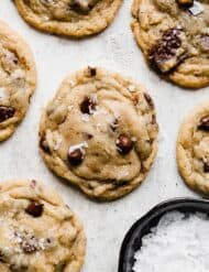 The Best Chocolate Chip Cookies topped with sea salt on a gray background.