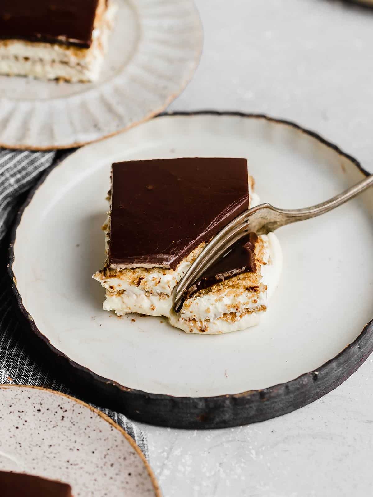 A square slice of Chocolate Eclair Cake on a black rimmed white plate.