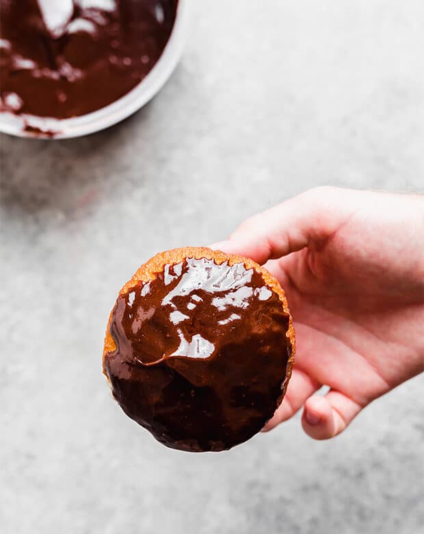 A hand holding a freshly chocolate glazed dipped donut.