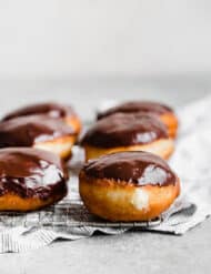 Boston Cream Donuts covered in a chocolate glaze sitting on a cooling rack.