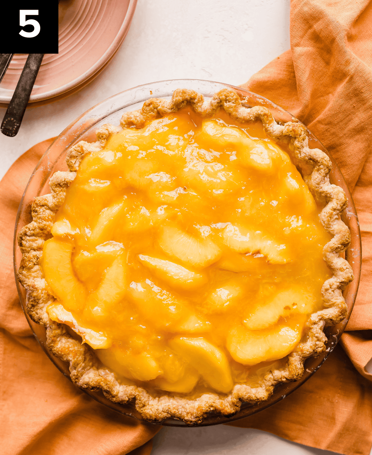 Peach pie in a butter pie crust on a peach colored napkin on a white background.