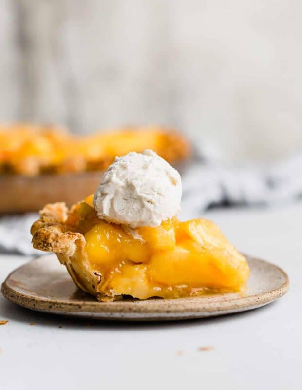 A slice of peach pie topped with a scoop of vanilla ice cream, against a white background.