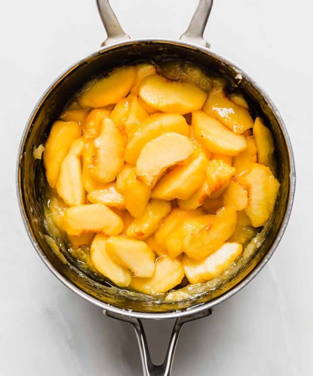 Sliced peaches in a saucepan against a white background.