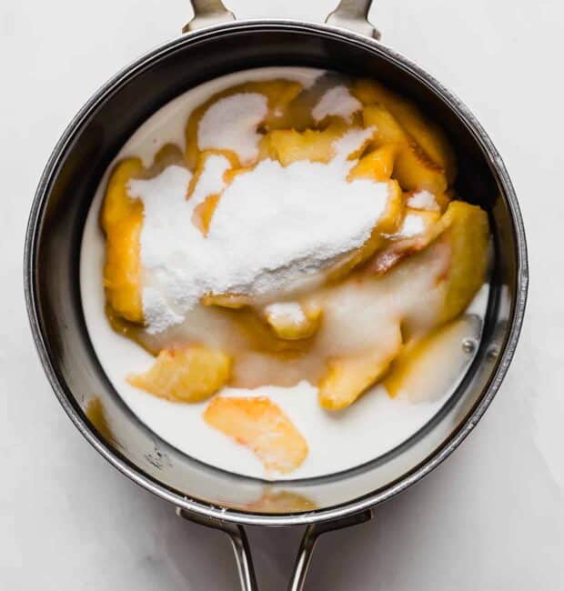 A saucepan with sliced peaches, sugar, and a cornstarch slurry.