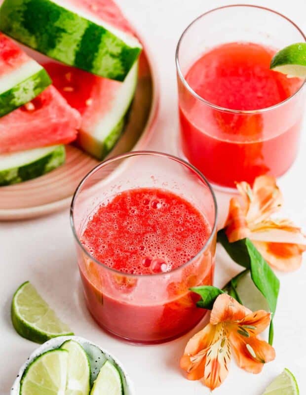 Two glasses of watermelon lime juice with sliced watermelon in the background.