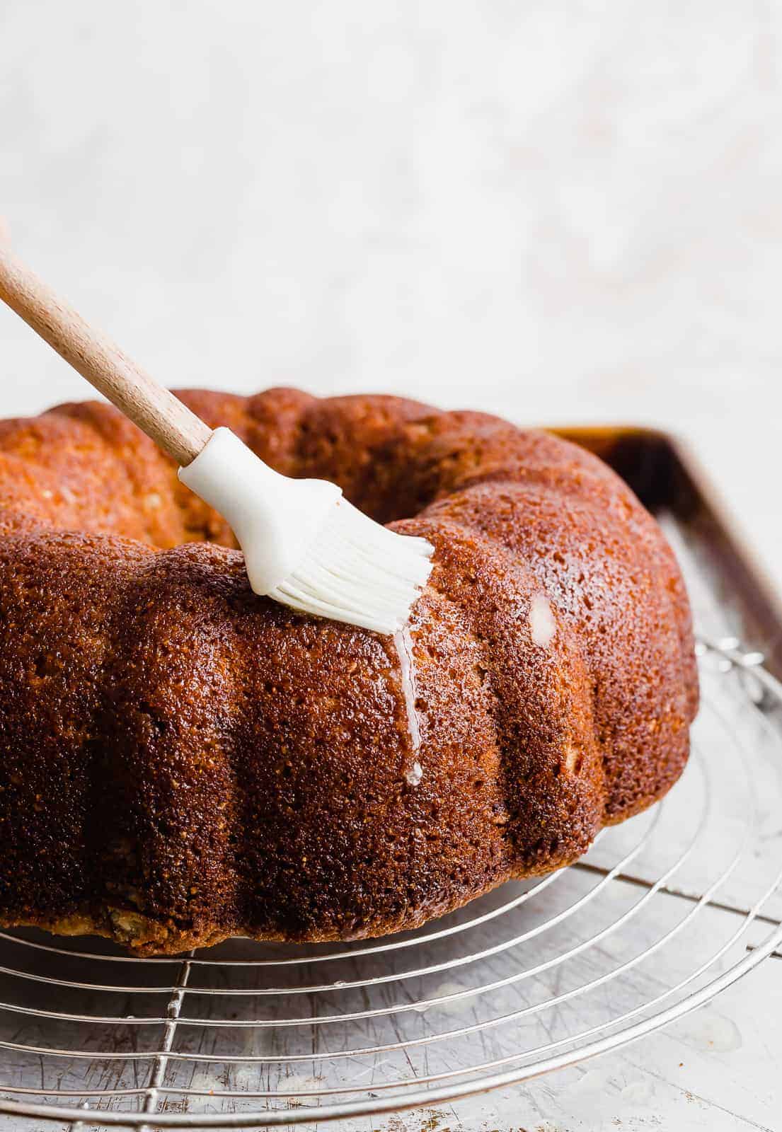 A white pastry brush spreading melted butter over a Bundt Cake.