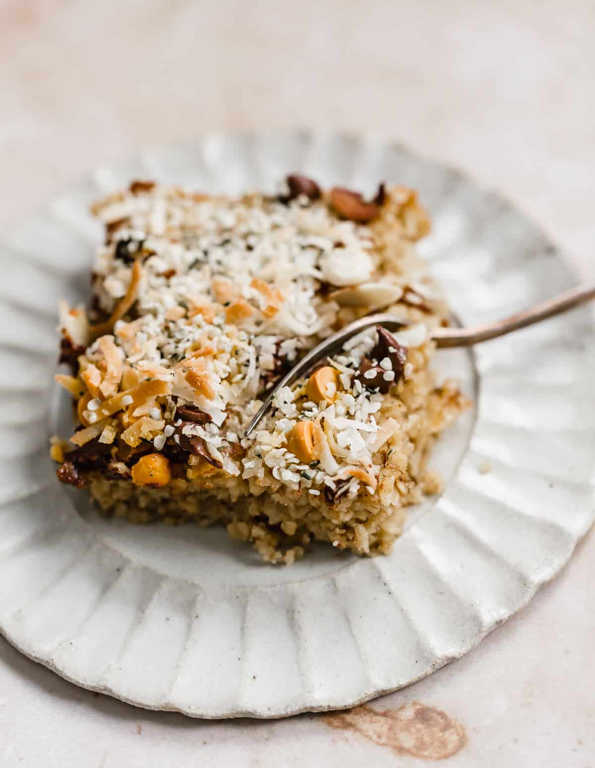 A square slice of Breakfast Baked Oatmeal Cake topped with butterscotch chips, coconut, hemp hearts, and chocolate chips.