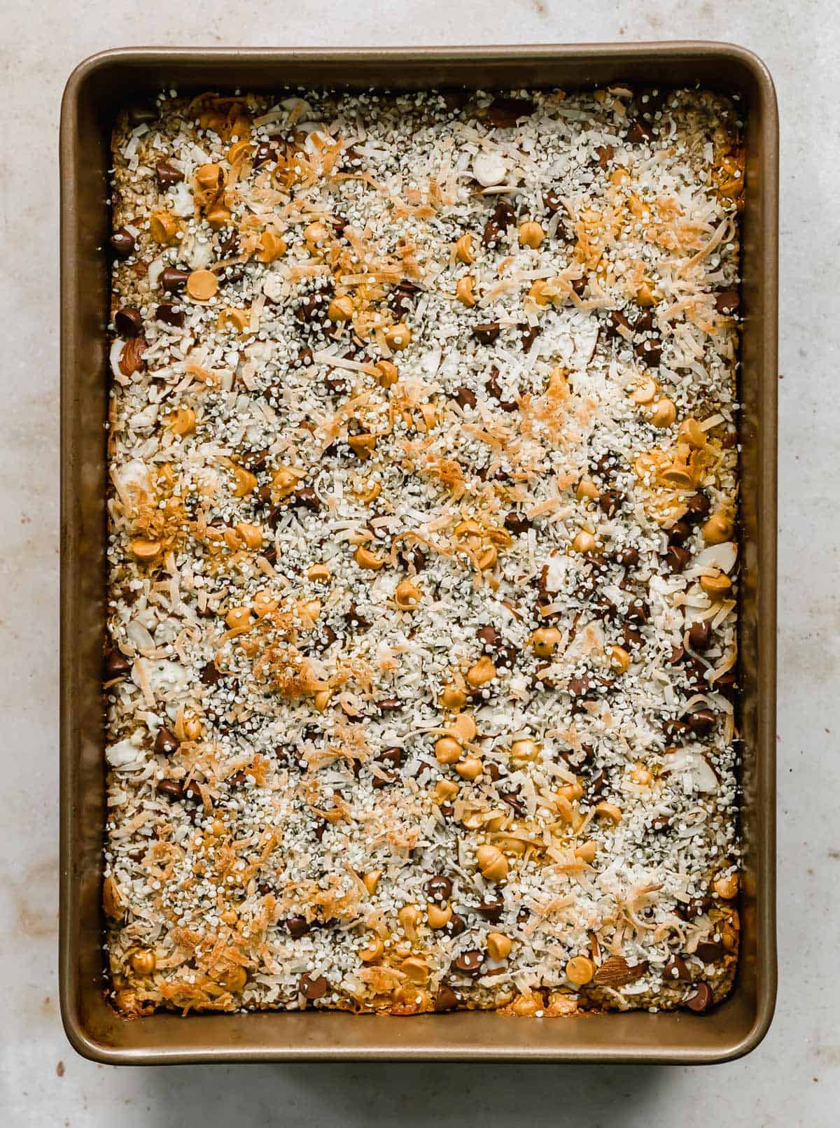 A Breakfast Baked Oatmeal Cake in a rectangular baking dish, topped with toasted coconut, chocolate chips, hemp hearts, and butterscotch chips.