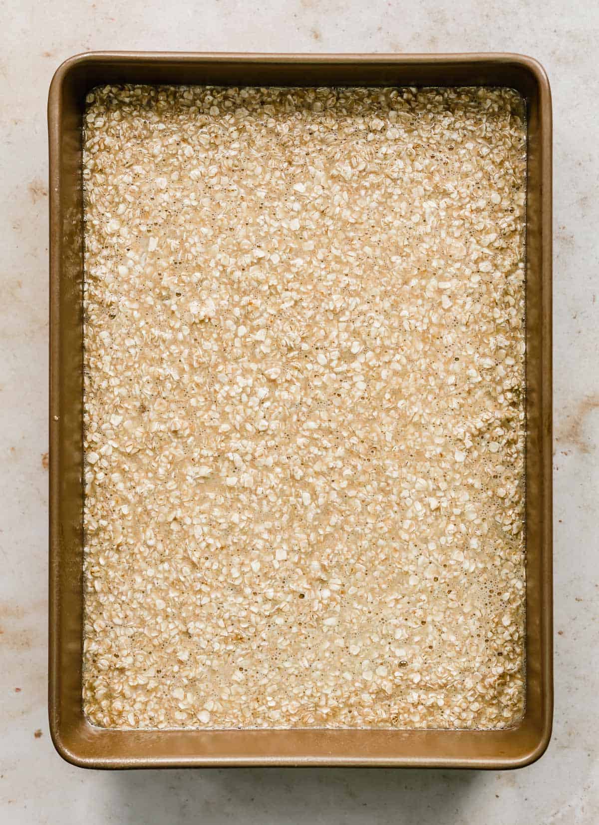 A bronze rectangular baking dish full of oatmeal cake batter.