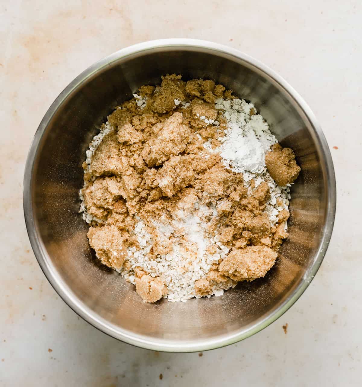 A metal bowl full of the dry ingredients used to make a baked oatmeal cake recipe.