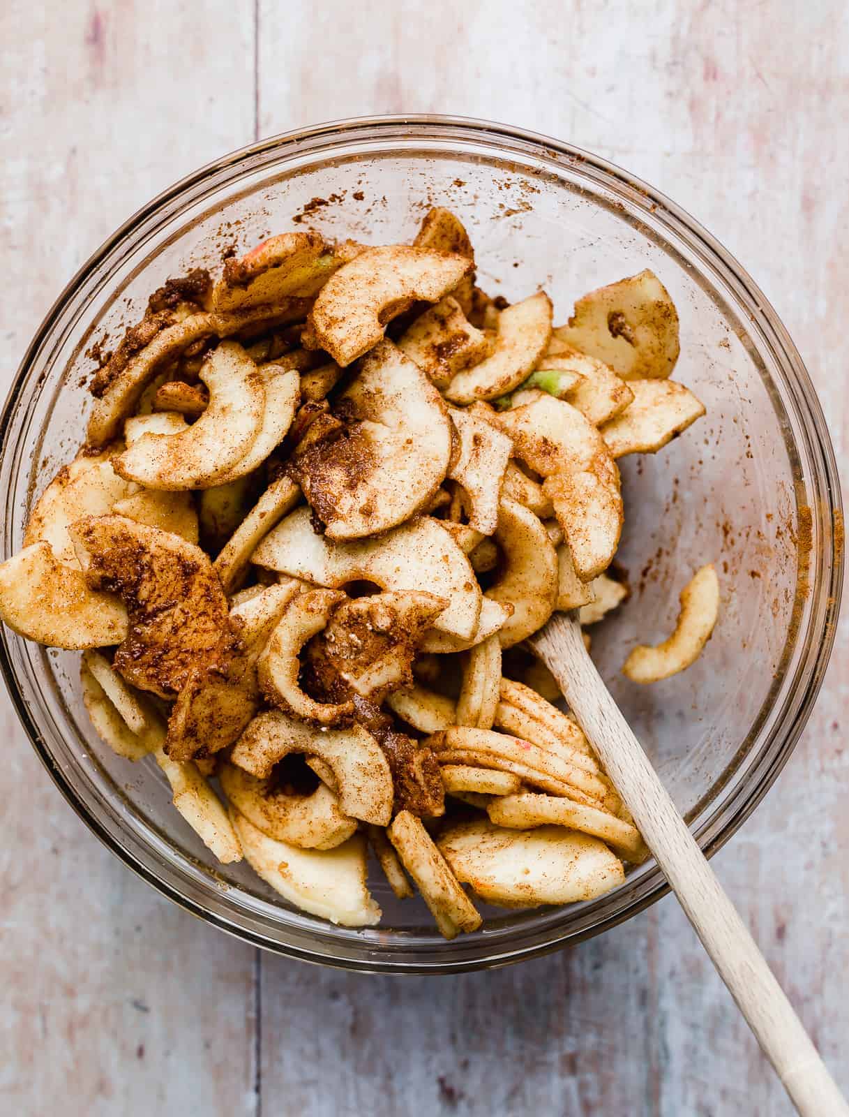 Glass bowl full of sliced apples tossed in brown sugar and ground cinnamon.