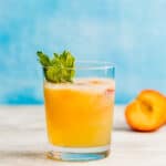 A glass full of peach punch in front of a blue background.