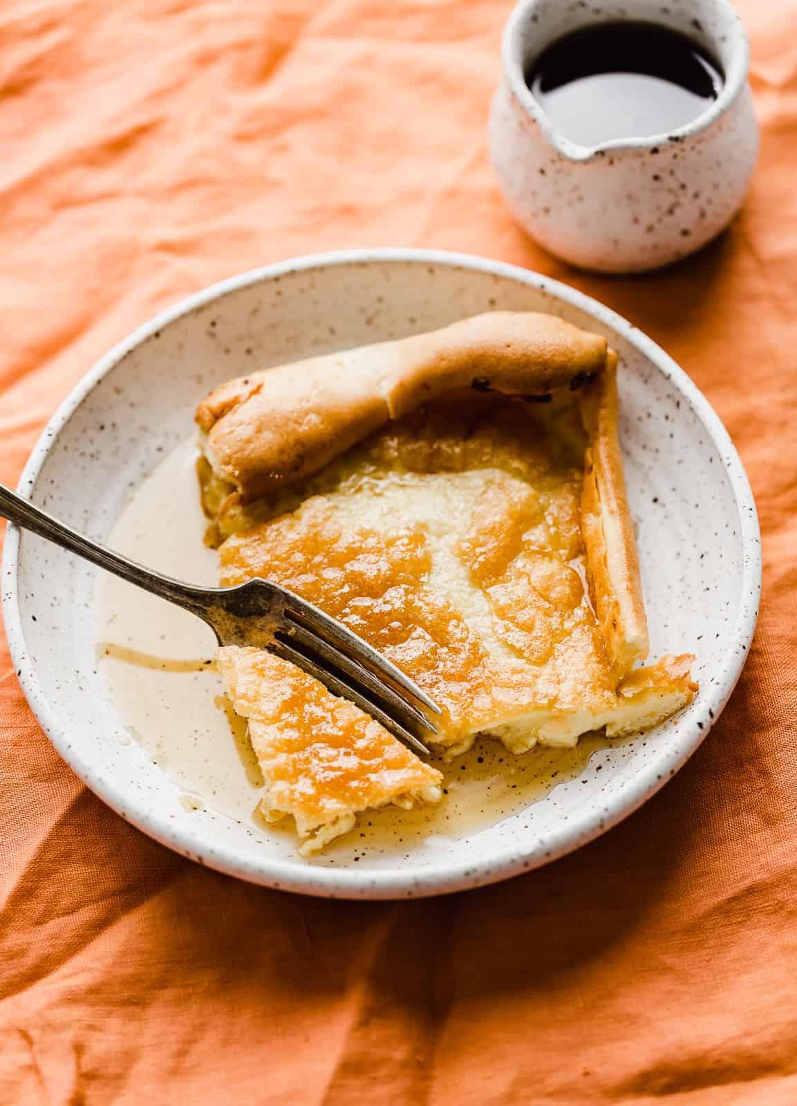 A slice of a German Pancake on a white plate with syrup over the pancake.