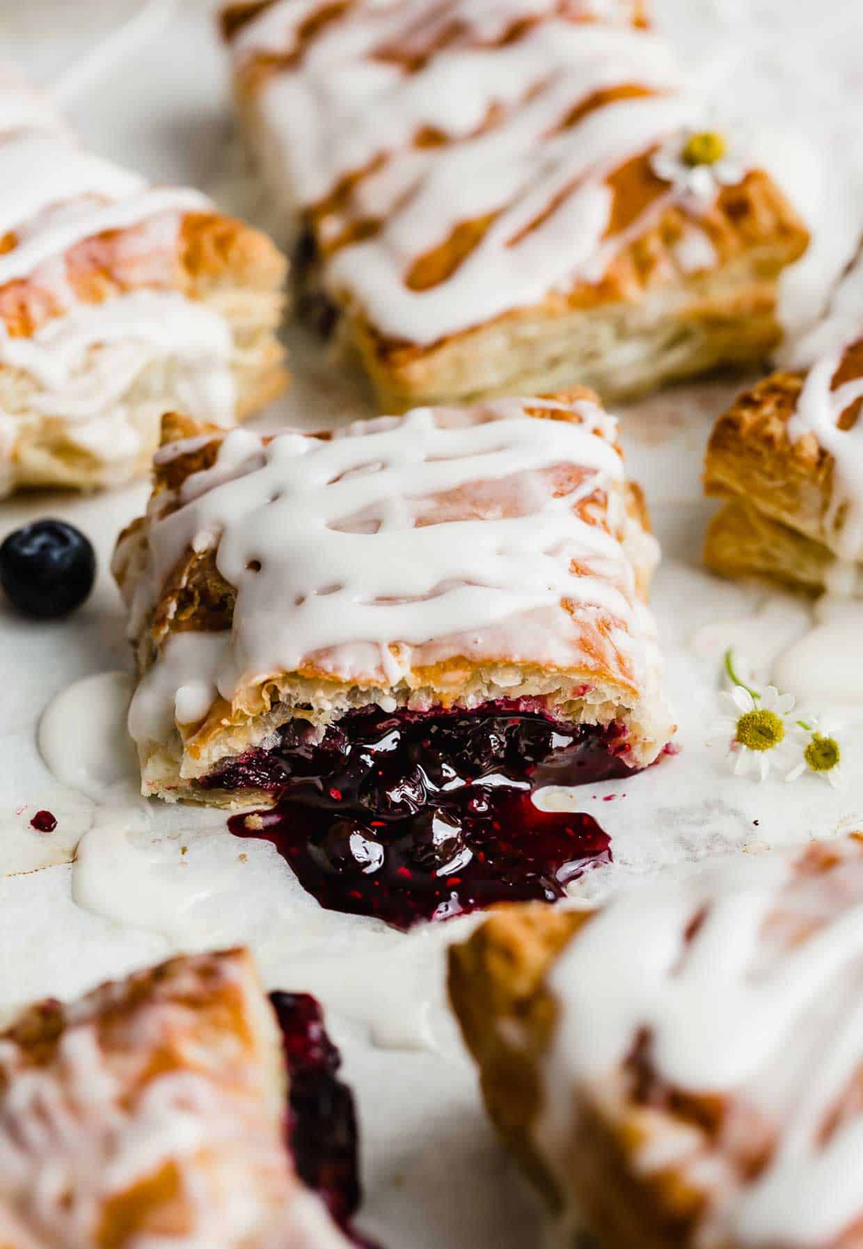 A Homemade Toaster Strudel that has been cut in half and has the triple berry jam spilling on to the white table.