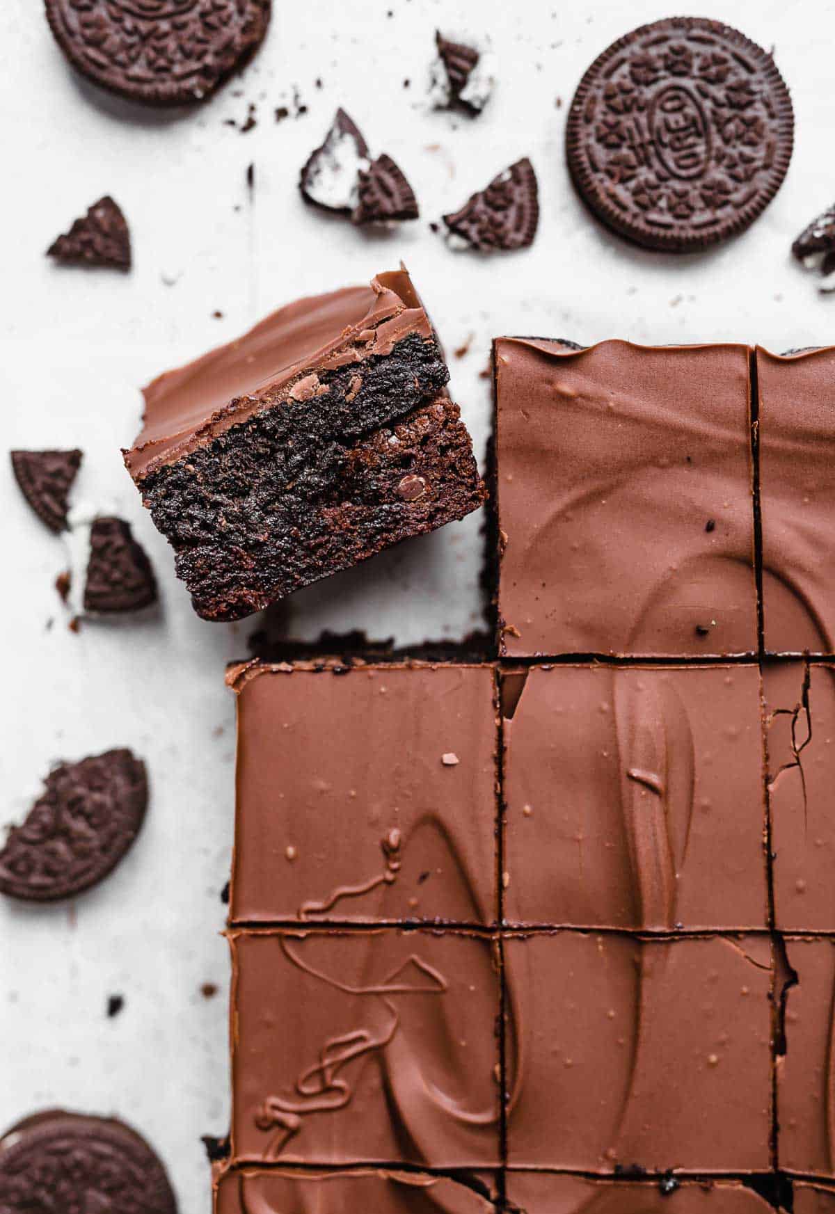 An Oreo Truffle Brownie on a white background with oreo crumbs scattered around it.