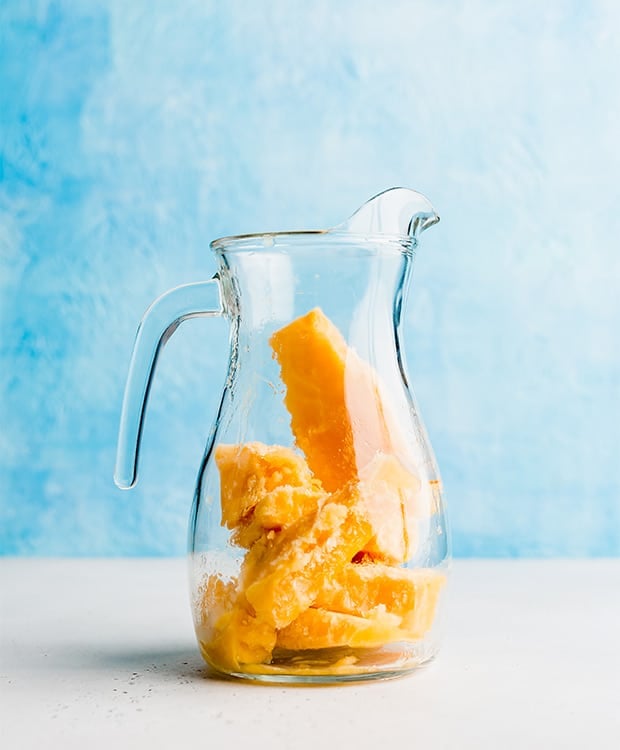 A glass pitcher with frozen peach punch chunks in it.