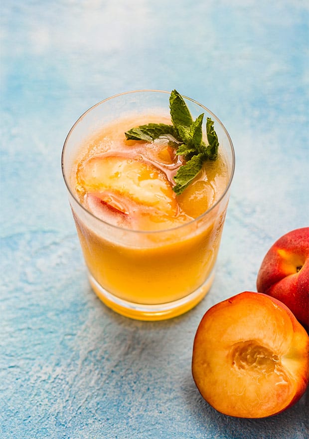 A glass of peach punch with a sprig of fresh mint in the glass.