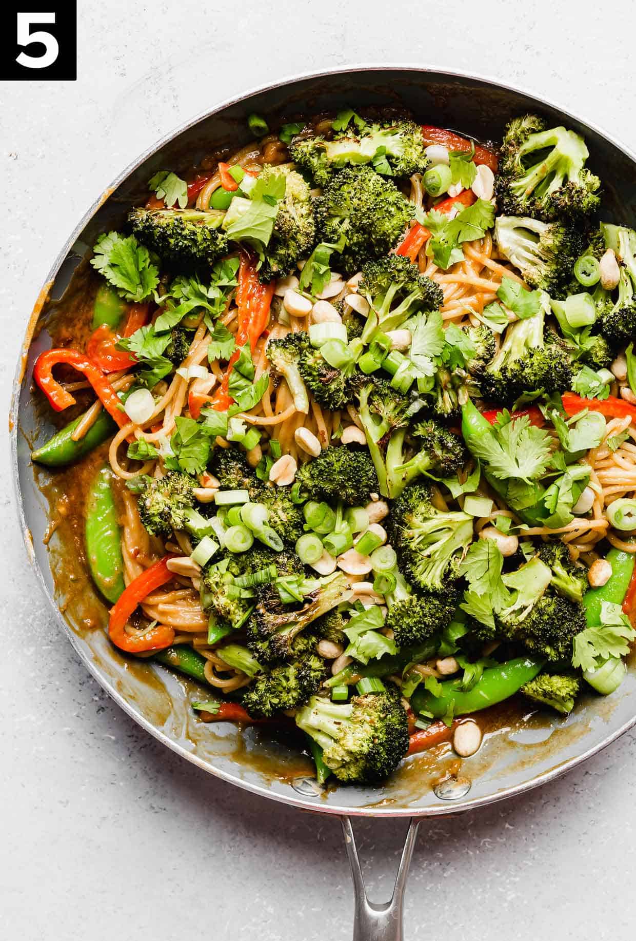 A skillet filled with roasted broccoli peanut butter noodles with vegetables.