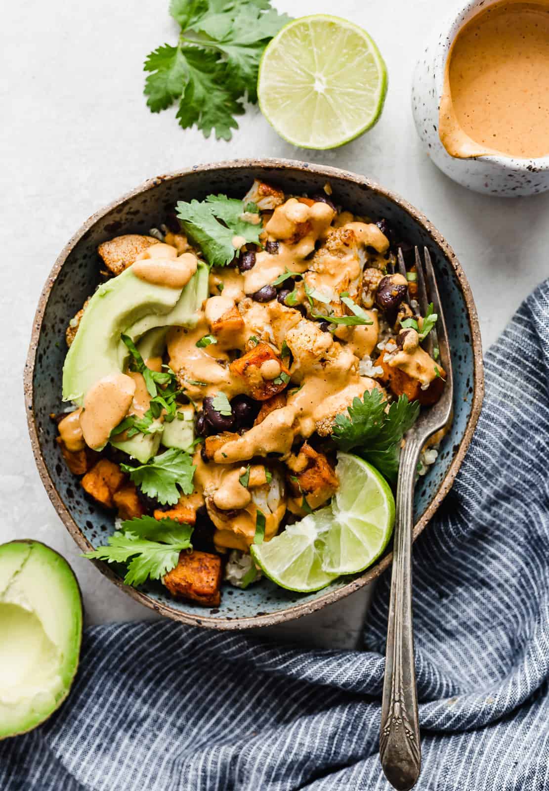 A blue bowl full of quinoa topped with roasted sweet potatoes and cauliflower.