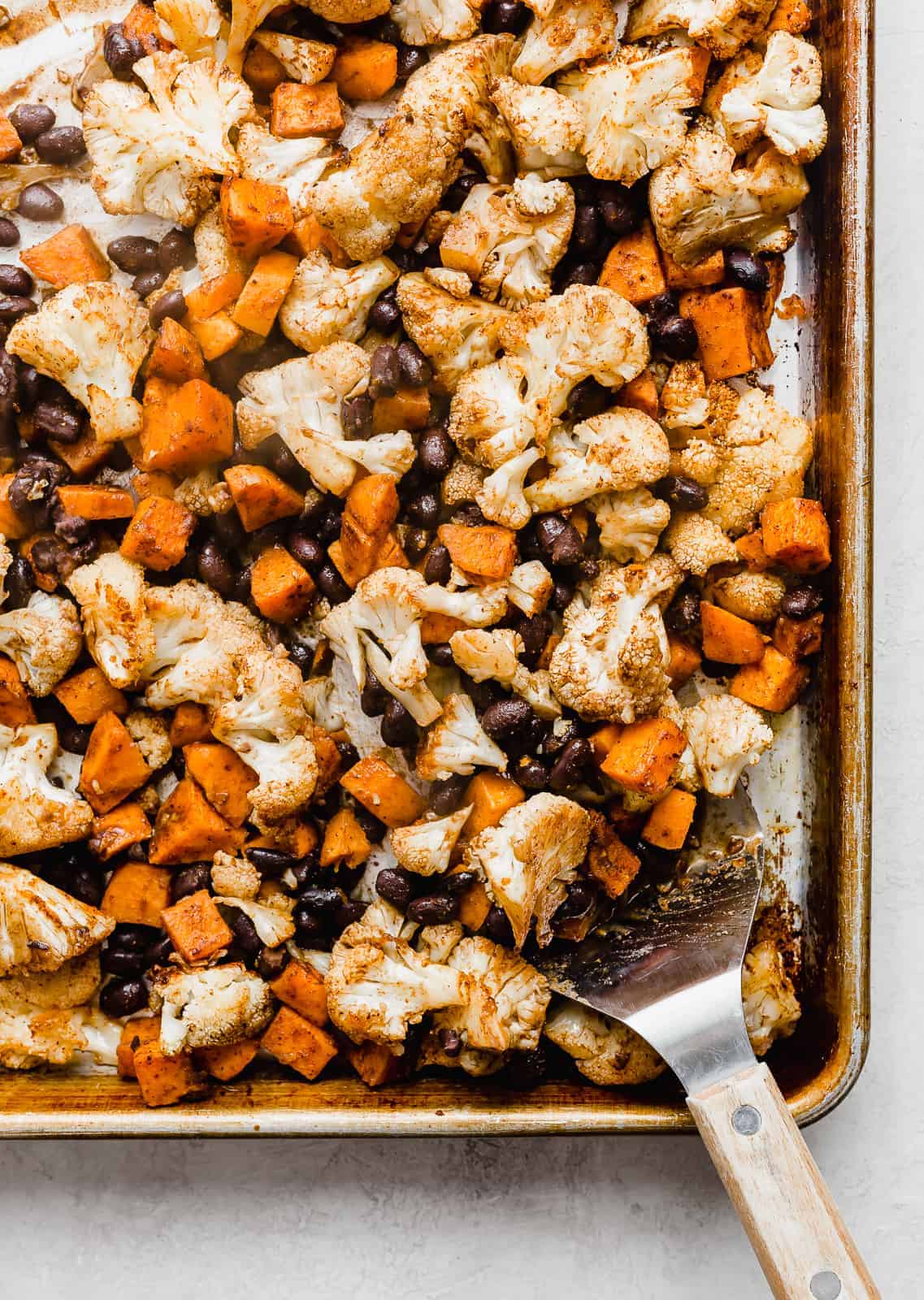 A sheet pan with black beans and roasted sweet potatoes and cauliflower. 