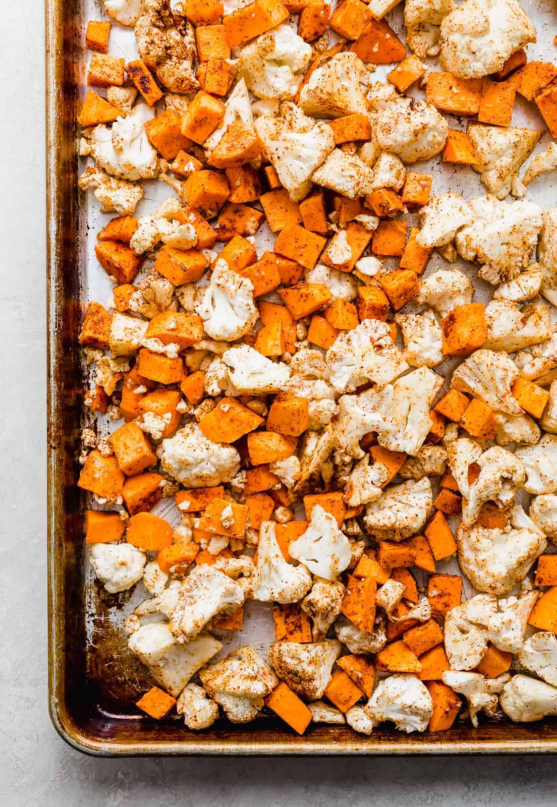 A sheet pan with chopped cauliflower and sweet potatoes on it.