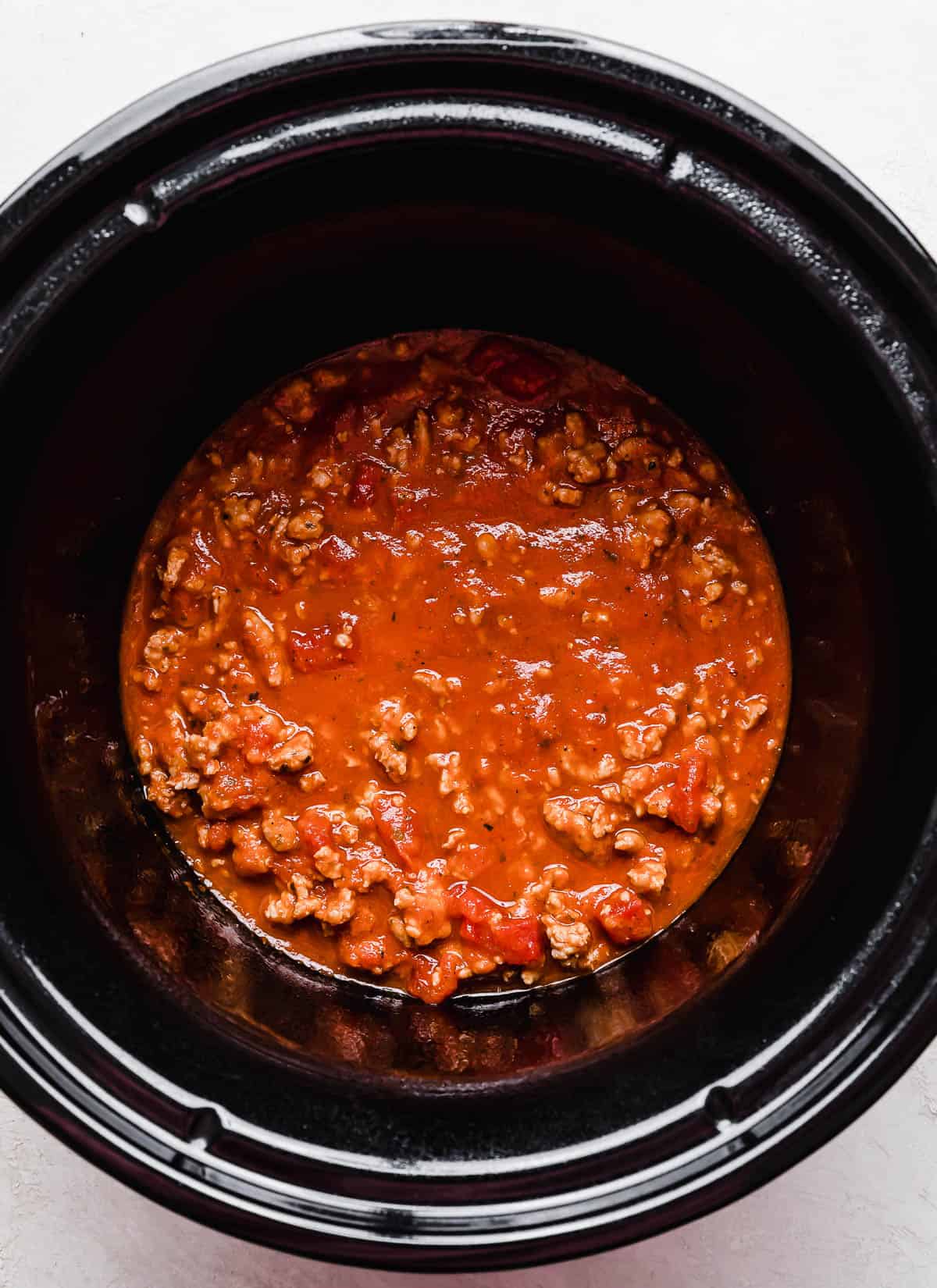 A round black crock pot with ground meat and red sauce in it.