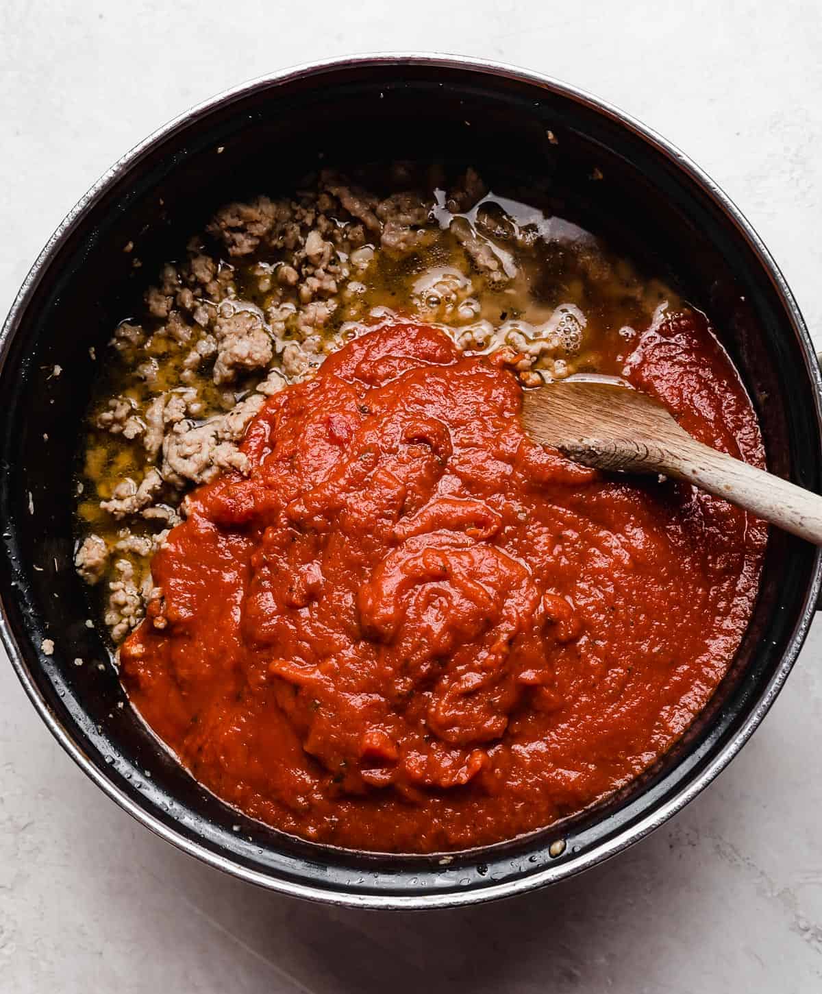 A pot with ground sausage and red marinara sauce in it.