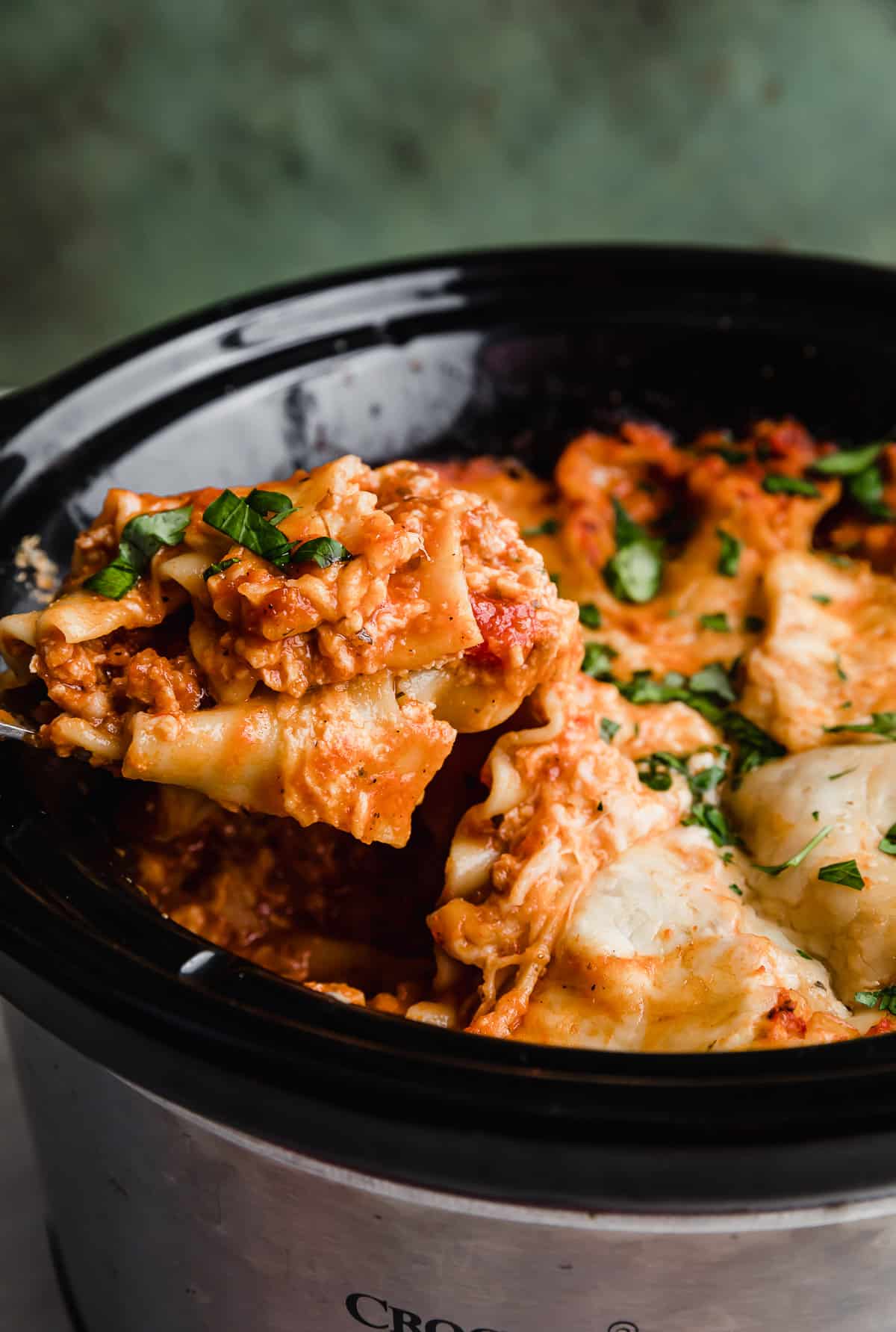 A serving spoon scooping out Slow Cooker Lasagna from a crock pot.