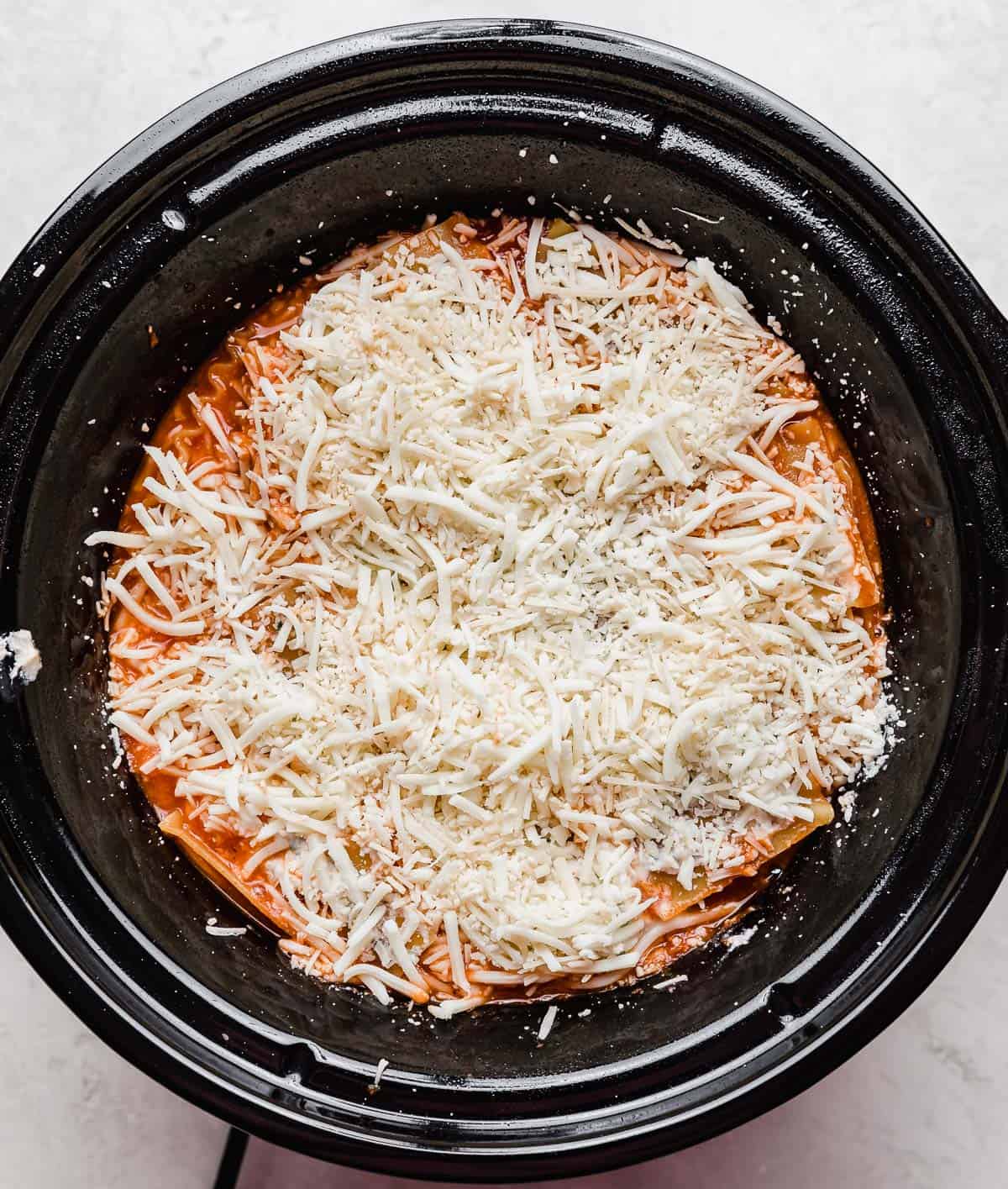Shredded mozzarella cheese overtop Slow Cooker Lasagna in a round crockpot.