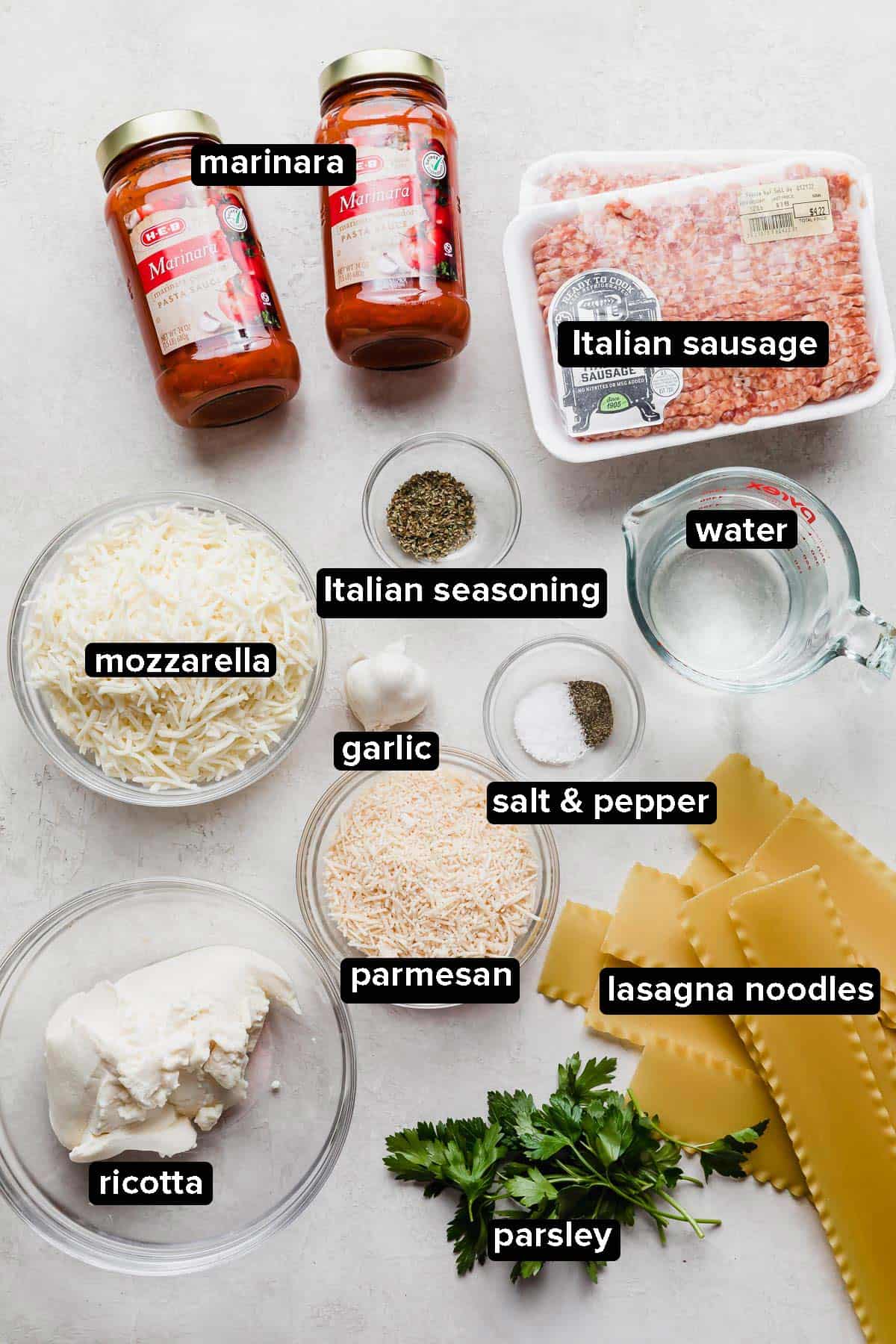 Slow Cooker Lasagna ingredients on a white background including jar sauce, ricotta, and uncooked lasagna noodles.