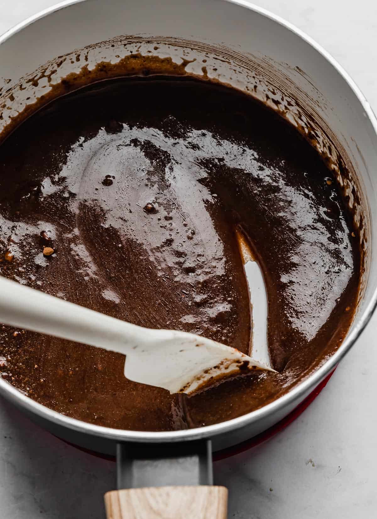 A white spatula stirring a chocolate mixture in a white pot.