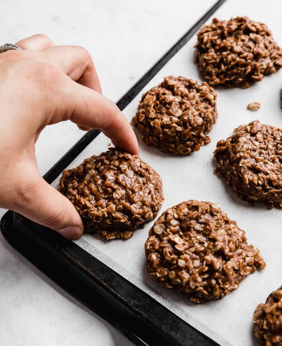 A hand grabbing a Chocolate Peanut Butter No Bake Cookies from a white parchment paper.