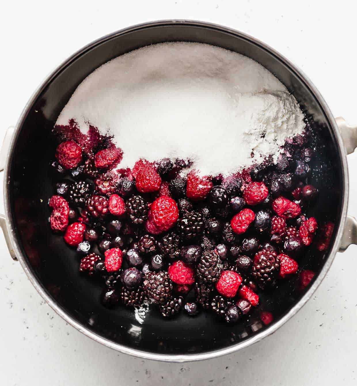 Mixed frozen berries and sugar in a black saucepan. 