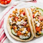 Two Chickpea Gyros on a white plate topped with cucumber, tomatoes, and feta cheese.