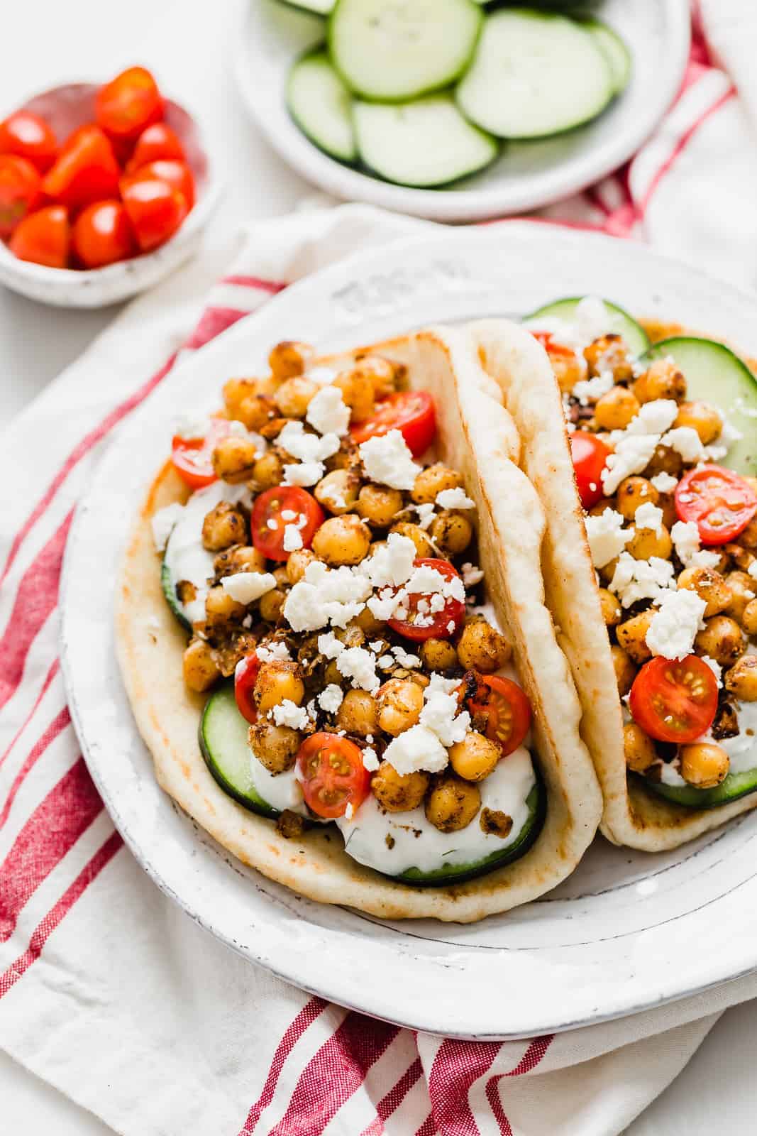 Two Chickpea Gyros on a white plate topped with cucumber, tomatoes, and feta cheese.