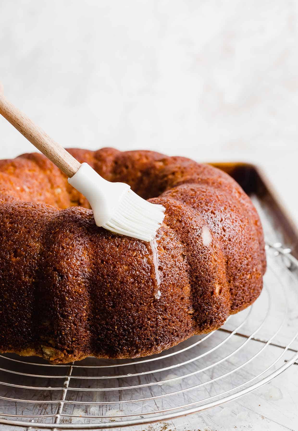 A white pastry brush spreading melted butter overtop a Apple Cider Bundt Cake.