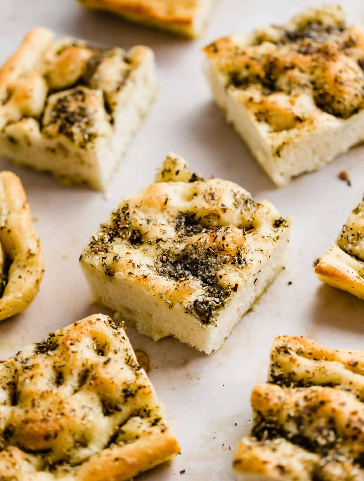 Focaccia Bread squares topped with fresh herbs on a light beige background.
