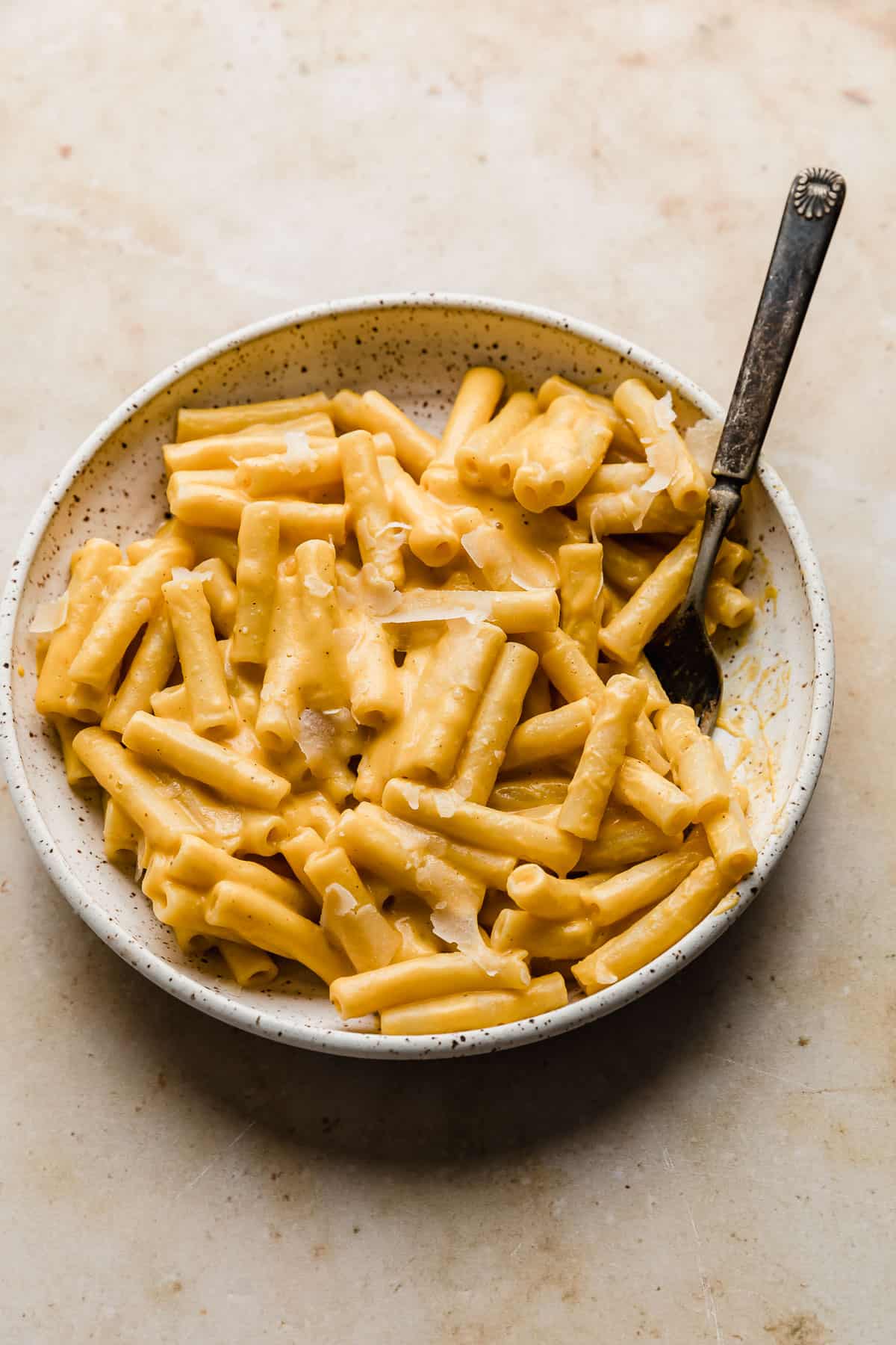 A white plate with butternut squash pasta sauce covered ziti noodles. 