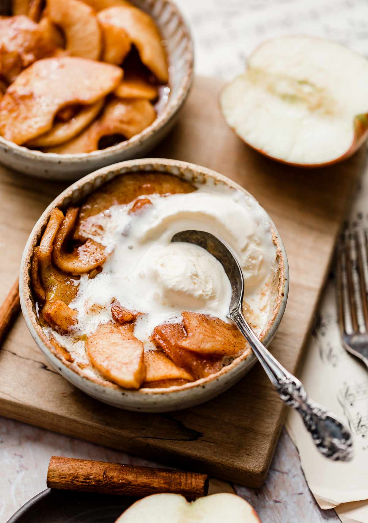 Cinnamon Baked Apples with peeled apples, in a white bowl topped with slightly melted vanilla ice cream.