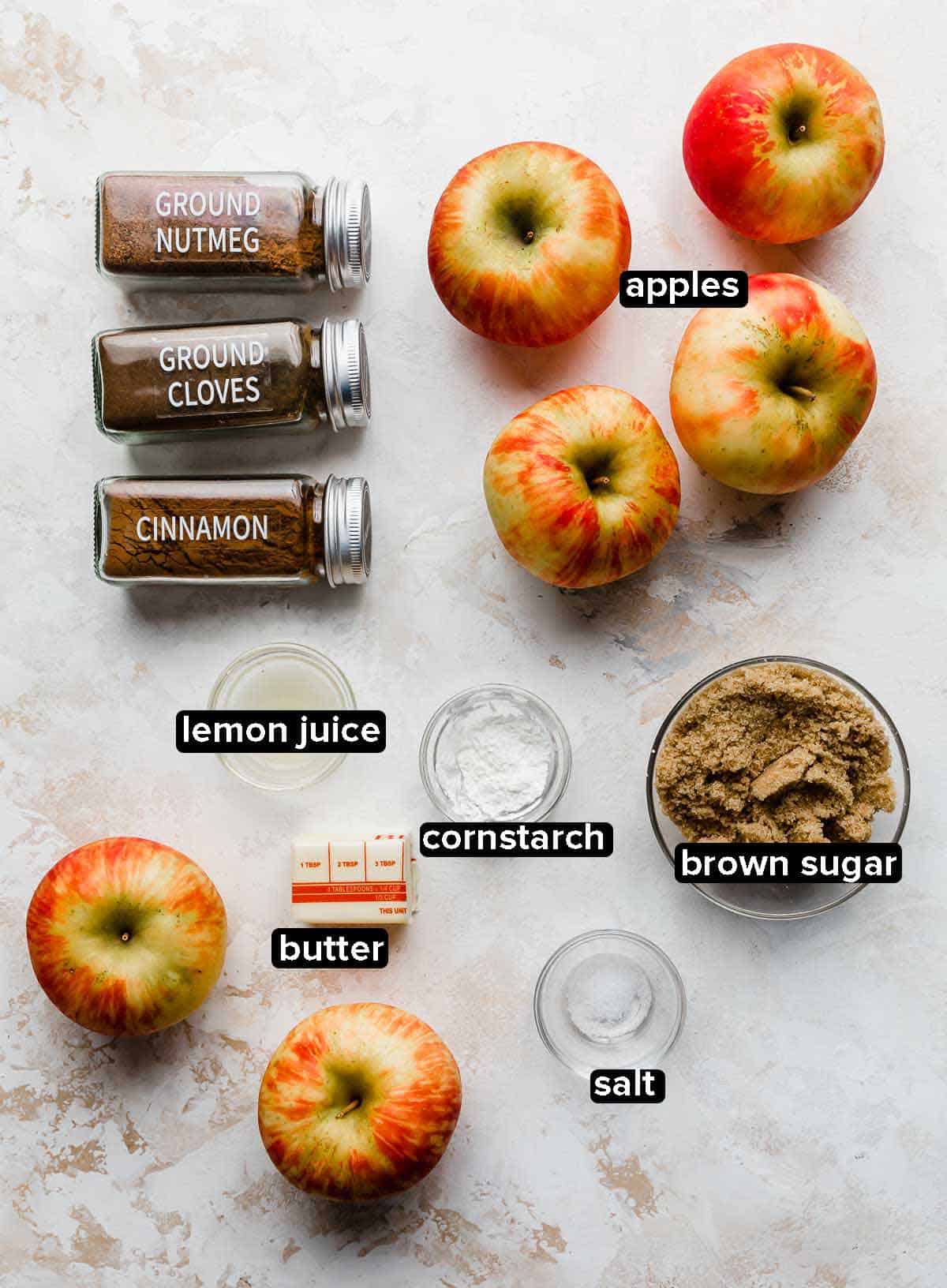 Cinnamon Baked Apples ingredients portioned into glass bowls on a cream textured background.