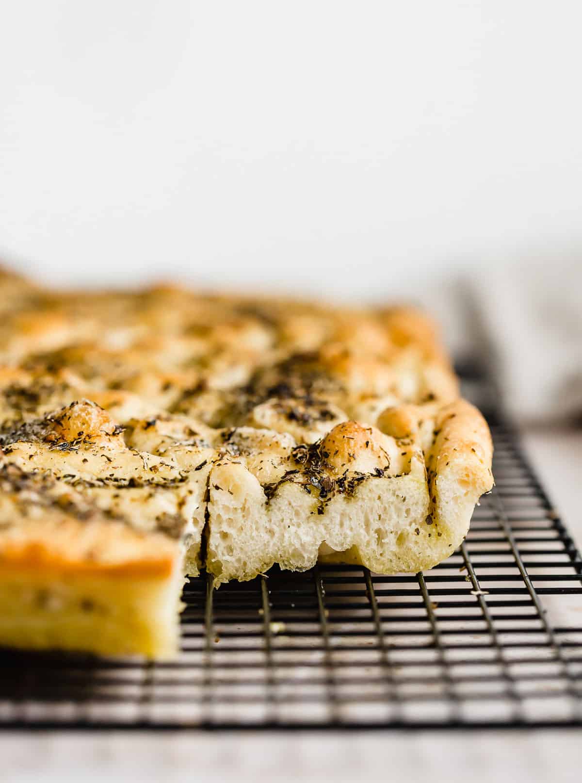 A side photo of a fluffy focaccia recipe showing the thick bread topped with herb olive oil.