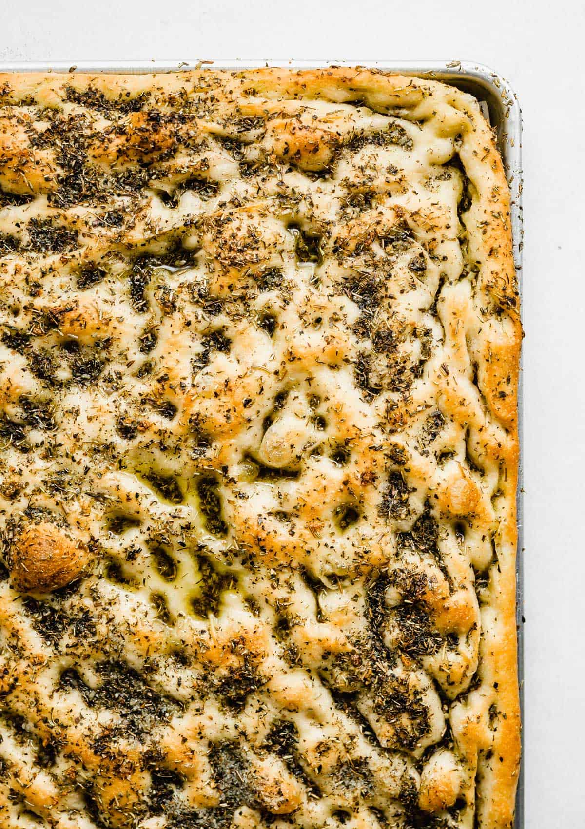Easy Focaccia Bread in a baking sheet topped with lots of herbs, baked until golden brown on top. 